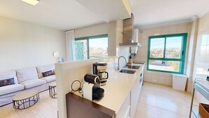 Una cocina moderna con horno empotrado, cafetera y lavabo. Hay una encimera blanca y una ventana con vistas a la ciudad.