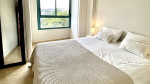 A bedroom with a large bed, a window with a view, and a door leading to another room.