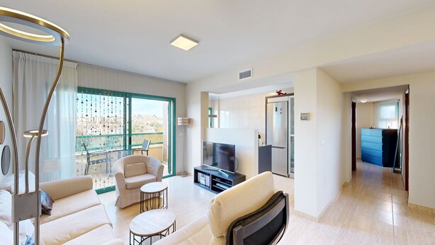 A modern living room with a sofa, armchair, TV, and a balcony with a city view.