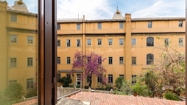A courtyard with a yellow building, a wooden staircase, and a tree with purple flowers.