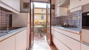 A modern kitchen with white cabinets, a gas stove, and a view through an open door to an outdoor patio with a table and chairs.