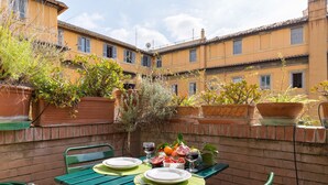 An outdoor dining area with a table set for two, surrounded by potted plants and a brick wall.