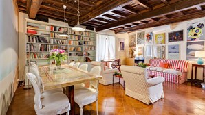 A spacious living room with a high ceiling, a large bookshelf, a dining area with a glass table, and a striped sofa.