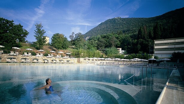 A swimming pool with lounge chairs and umbrellas, surrounded by trees and a mountain in the background.