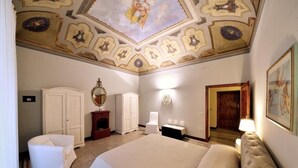 A spacious bedroom with a large bed, a wardrobe, a mirror, and a ceiling with decorative artwork.