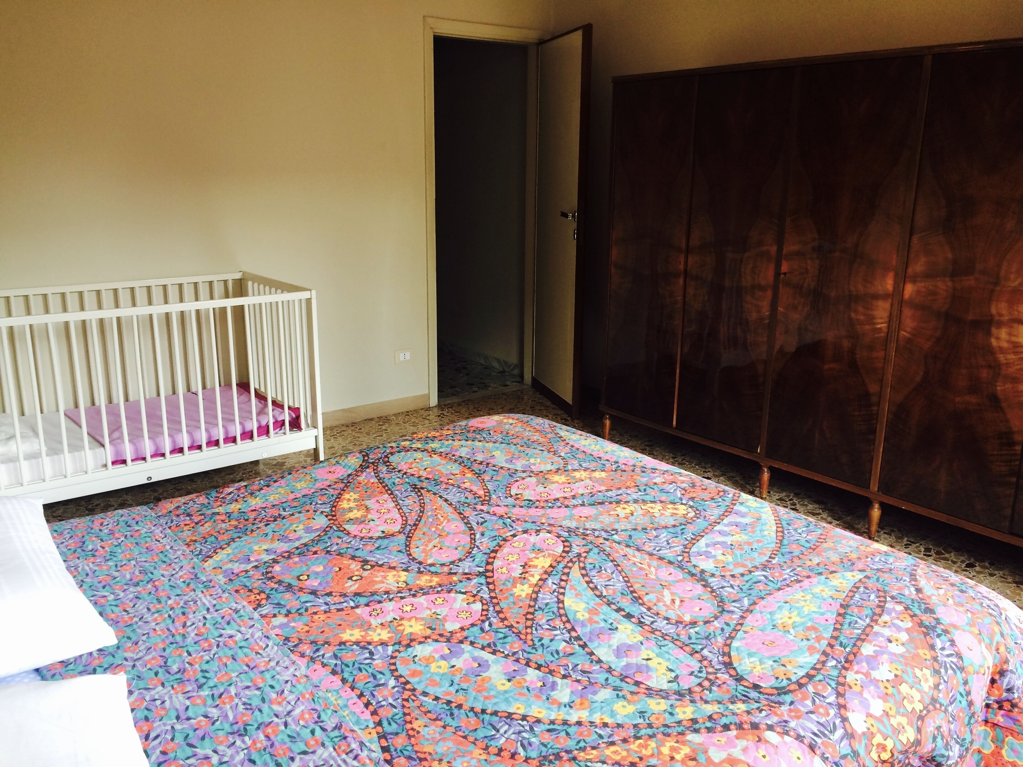 Ein Zimmer mit einem Babybett, einem gemusterten Teppich und einem dunklen Holzschrank.
