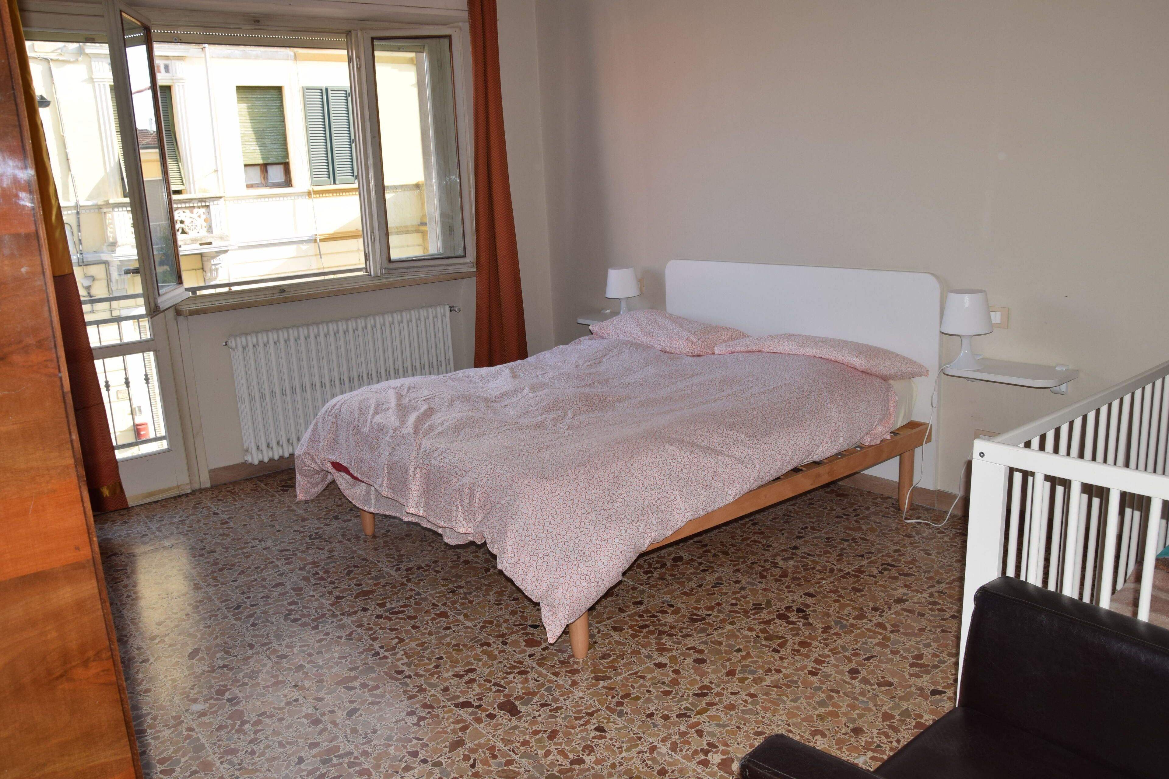 Un dormitorio con cama, ventana, radiador y cuna.