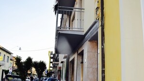 Un carrer estret amb cotxes aparcats i un edifici groc amb un balcó.