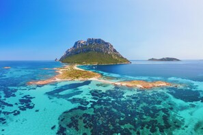 Vista aérea de una isla costera con aguas azul turquesa, un pico rocoso destacado y una pequeña zona de playa.