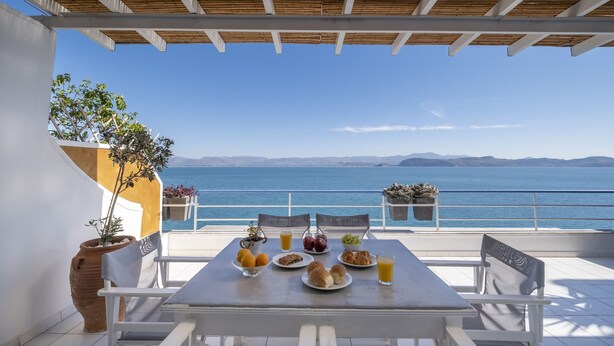 Una mesa dispuesta con comida y bebidas en un balcón con vistas al mar.