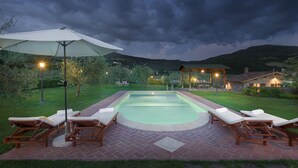A swimming pool with lounge chairs and an umbrella, surrounded by a brick patio and greenery. - Vinciluna 4, Emma Villas (Scanizza)