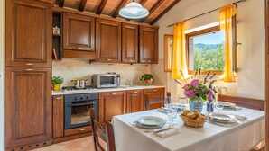 A kitchen with wooden cabinets, a stove, a microwave, and a dining area with a table set for two. - Vinciluna 4, Emma Villas (Scanizza)