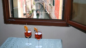 Due bicchieri di bevanda rossa con fettine d'arancia su un tavolo vicino a una finestra che si affaccia su un canale e palazzi.