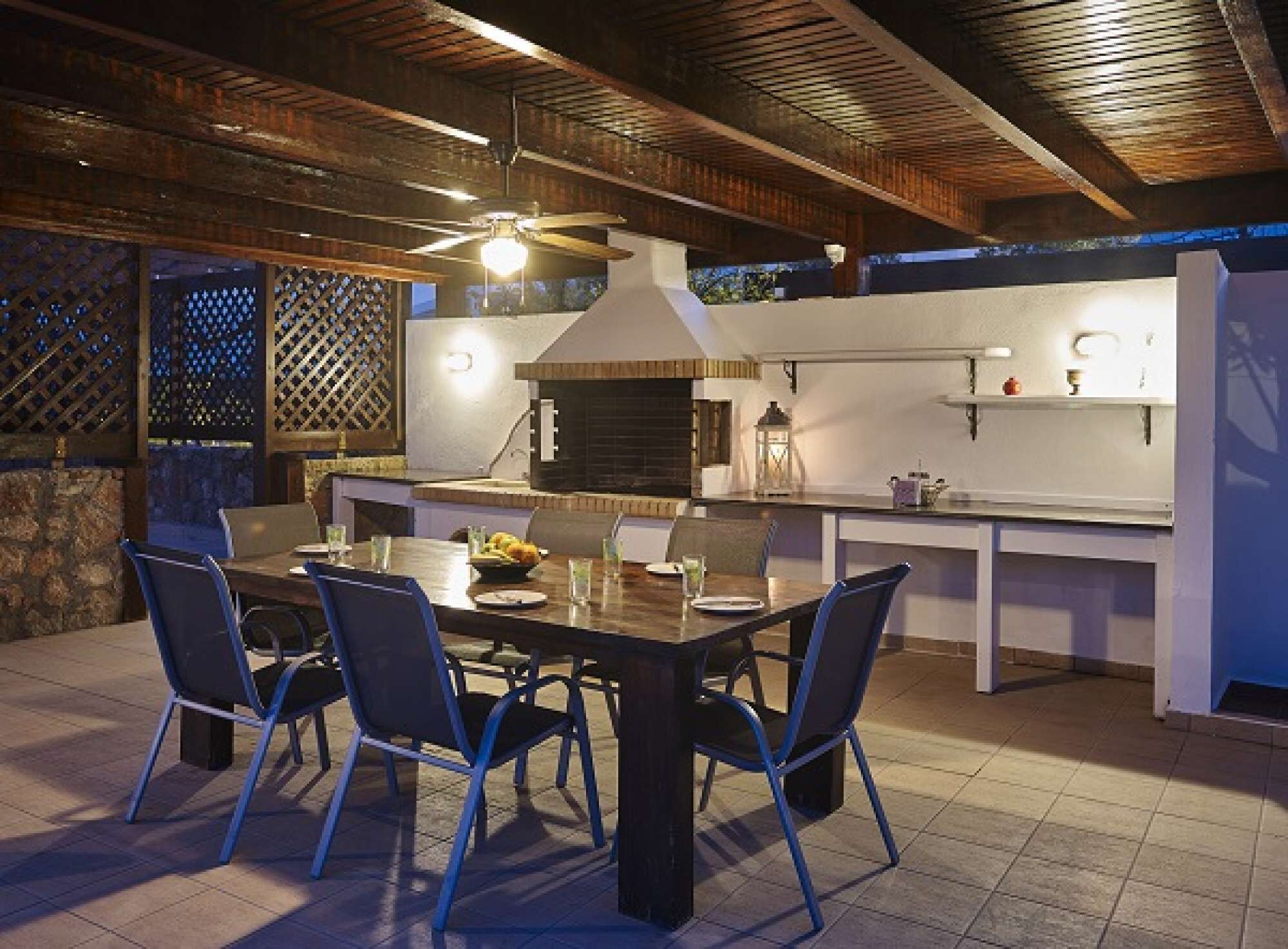 Una cocina exterior con mesa y sillas, una chimenea de ladrillo y una lámpara colgante.