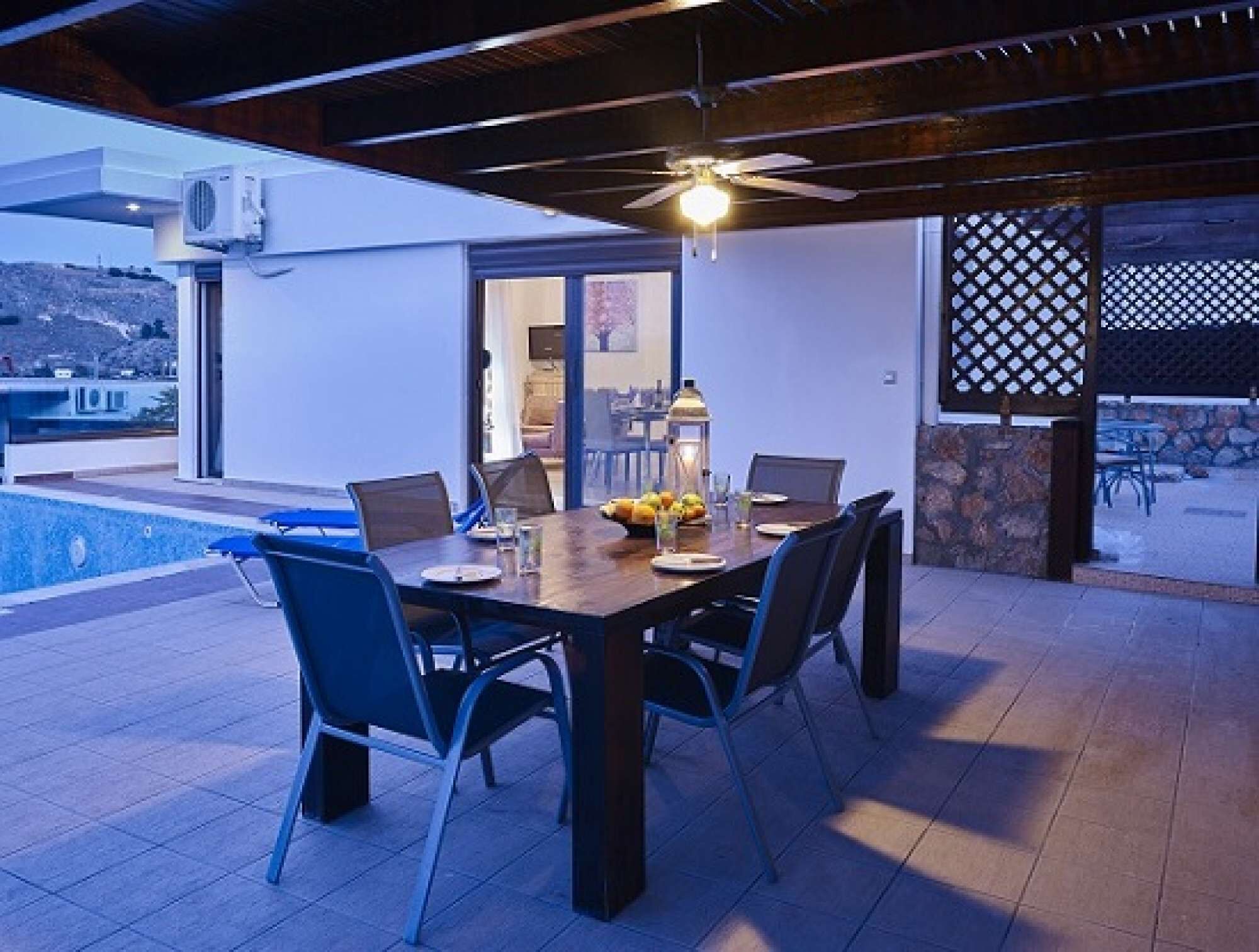 Un espace extérieur aménagé pour les repas, avec une piscine, un ventilateur de plafond et une vue sur le paysage.