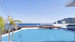 Piscina no terraço com vista ampla do oceano e paisagem montanhosa ao longe.