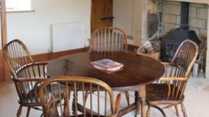 A dining area with a round wooden table surrounded by four wooden chairs, a fireplace, and a window with a view of the outside. - Far Reaching Rural Views- Pet Friendly  (Silsden)