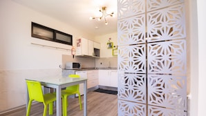 A modern kitchen with a dining area, featuring a glass table, bright chairs, and a decorative white partition. - Studio south lower-level w/ kitchenett and patio (Madeira)