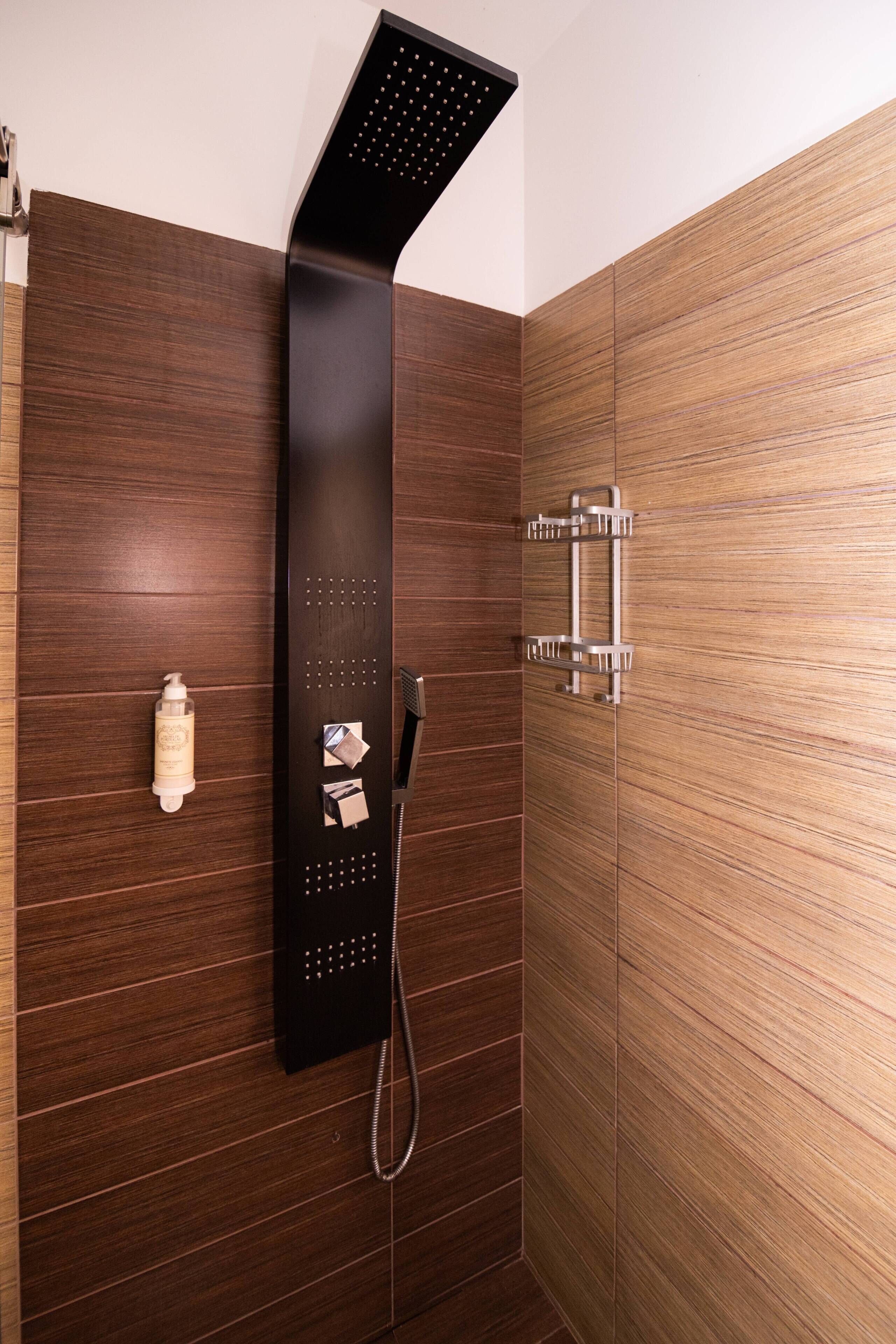 Una ducha moderna con un panel de control negro y elegante, un cabezal de ducha manual y un perchero.