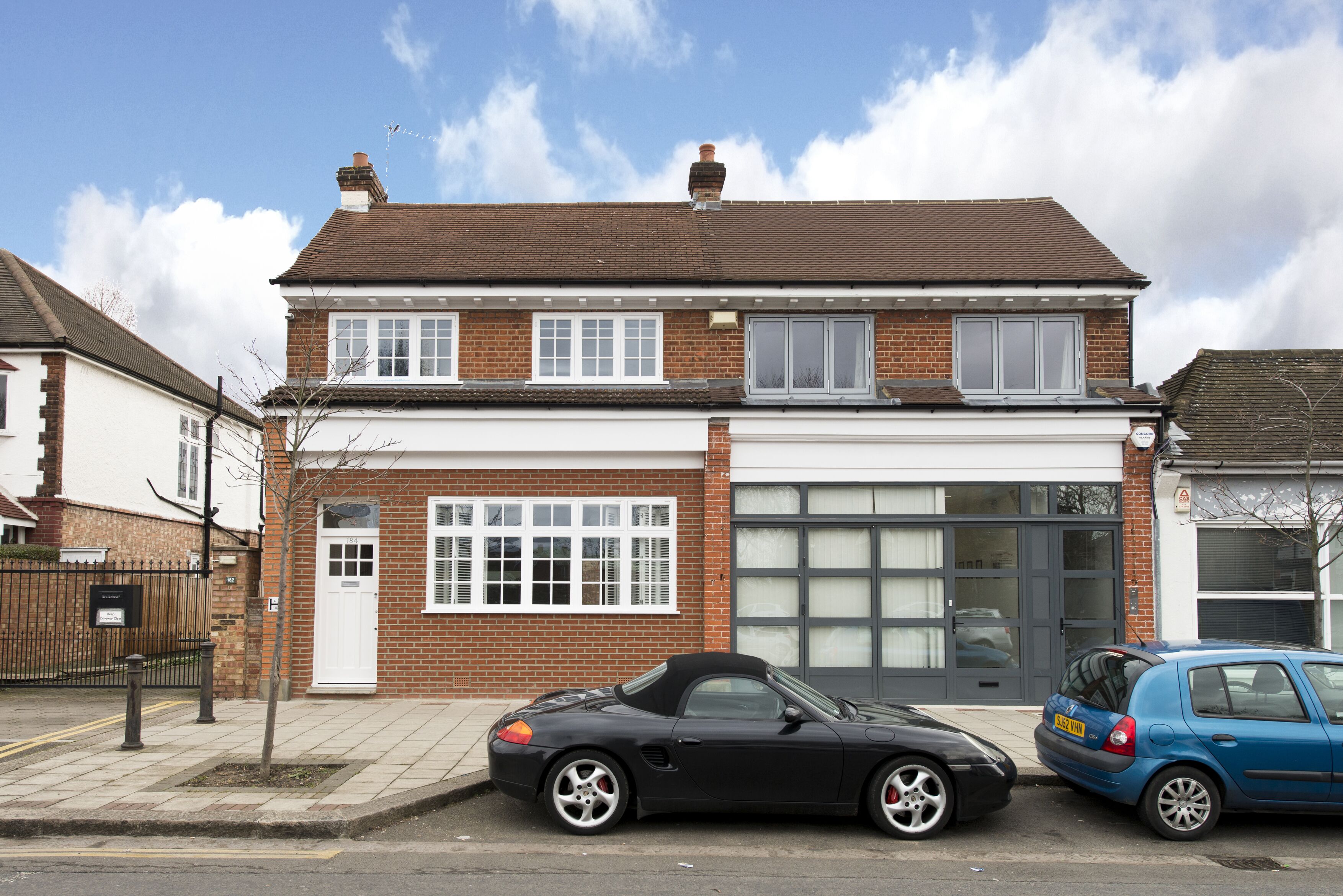 A two-story house with a garage, a black convertible, and a blue car parked in front.