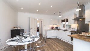 A modern kitchen with white cabinets, a wooden countertop, and a dining area with a round table and chairs. - London House, Chiswick, Luxurious, 3 Large Beds - 4 x Bath - GREAT PLACE TO STAY (London)