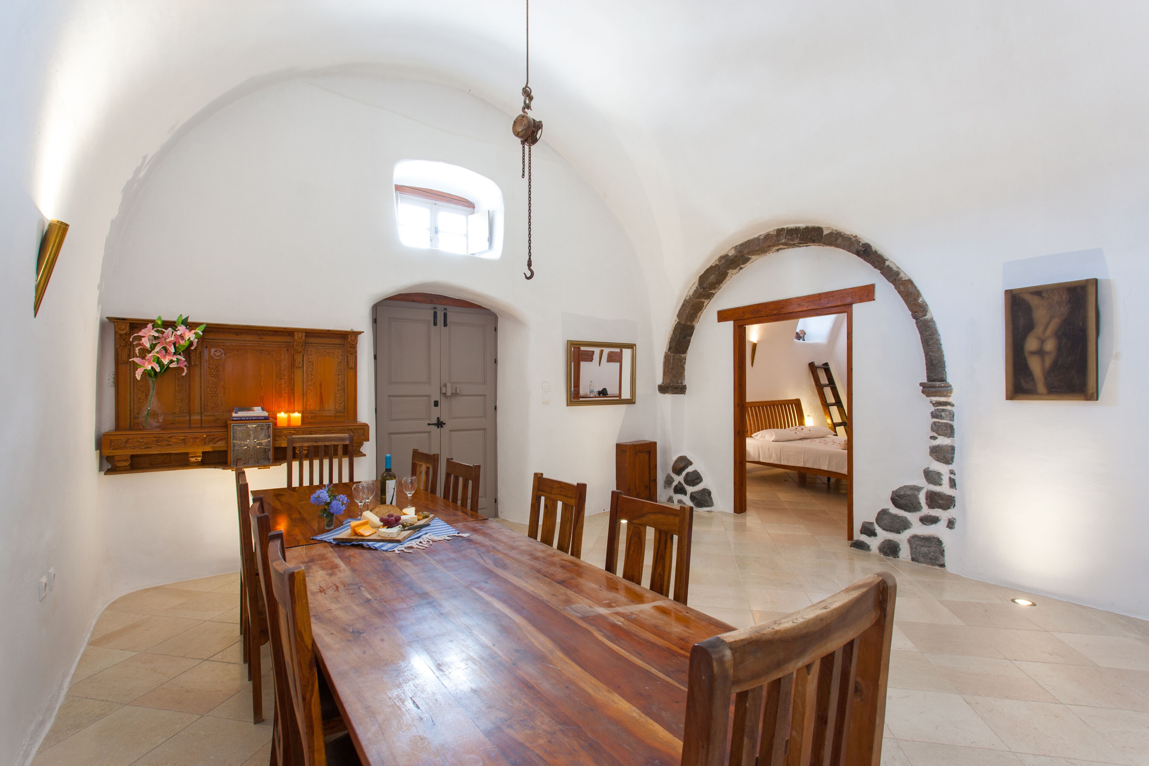 A spacious dining area with a long wooden table, surrounded by chairs, and a stone archway leading to another room.