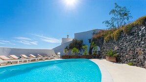 A swimming pool with lounge chairs, a stone wall, and a building with a white facade. - Spacious Luxury Private Villa - Heated Pool - Ocean Views (santorini)
