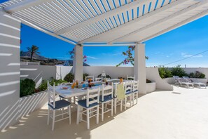 Un espace extérieur abrité, aménagé pour les repas, avec des meubles blancs et une pergola.