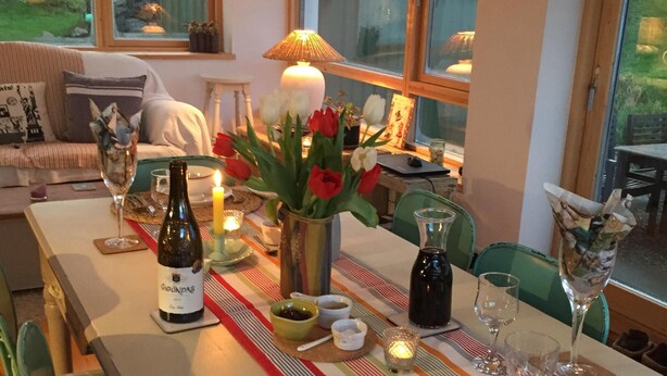 A dining table set with plates, glasses, and a bottle of wine, surrounded by chairs and a vase of flowers. - Traditional Failte Ireland 2025 Rustic Stone Cottage With Private River Fishing. (Clifden, Connemara)