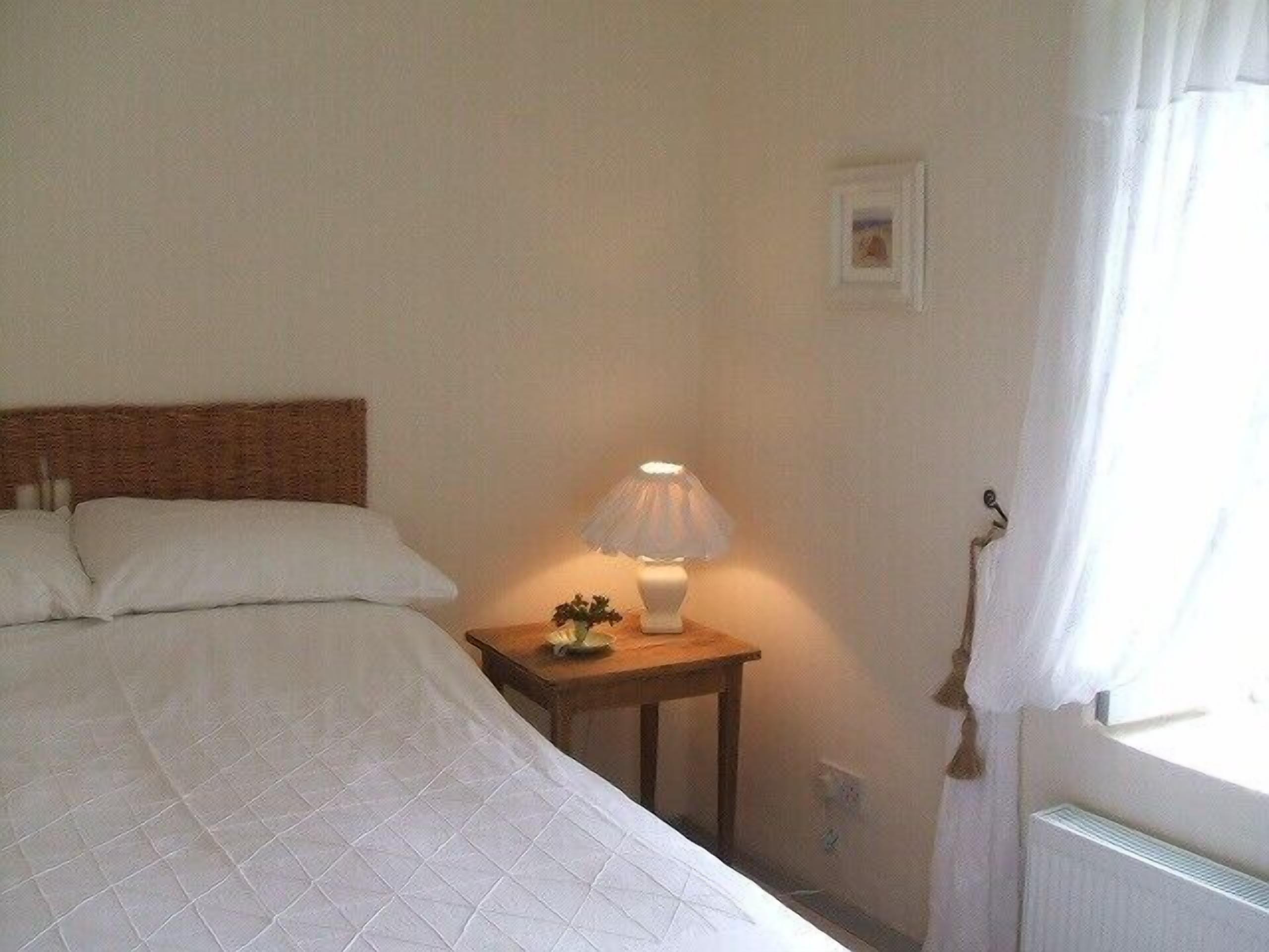 Un lit bien fait, recouvert d’une courtepointe matelassée, une table de chevet avec une lampe et un tableau encadré au mur.