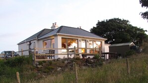 A house with a large porch, a fenced yard, and a barn in the background. - Traditional Failte Ireland 2025 Rustic Stone Cottage With Private River Fishing. (Clifden, Connemara)