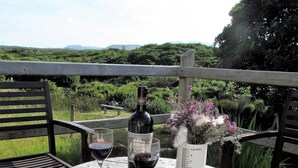 A round wooden table with a wine bottle and glasses, surrounded by chairs, set outdoors with a view of greenery and hills. - Traditional Failte Ireland 2025 Rustic Stone Cottage With Private River Fishing. (Clifden, Connemara)