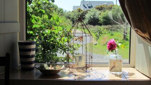 A window view with a potted plant, a metal birdcage, and a vase with a flower. - Traditional Failte Ireland 2025 Rustic Stone Cottage With Private River Fishing. (Clifden, Connemara)