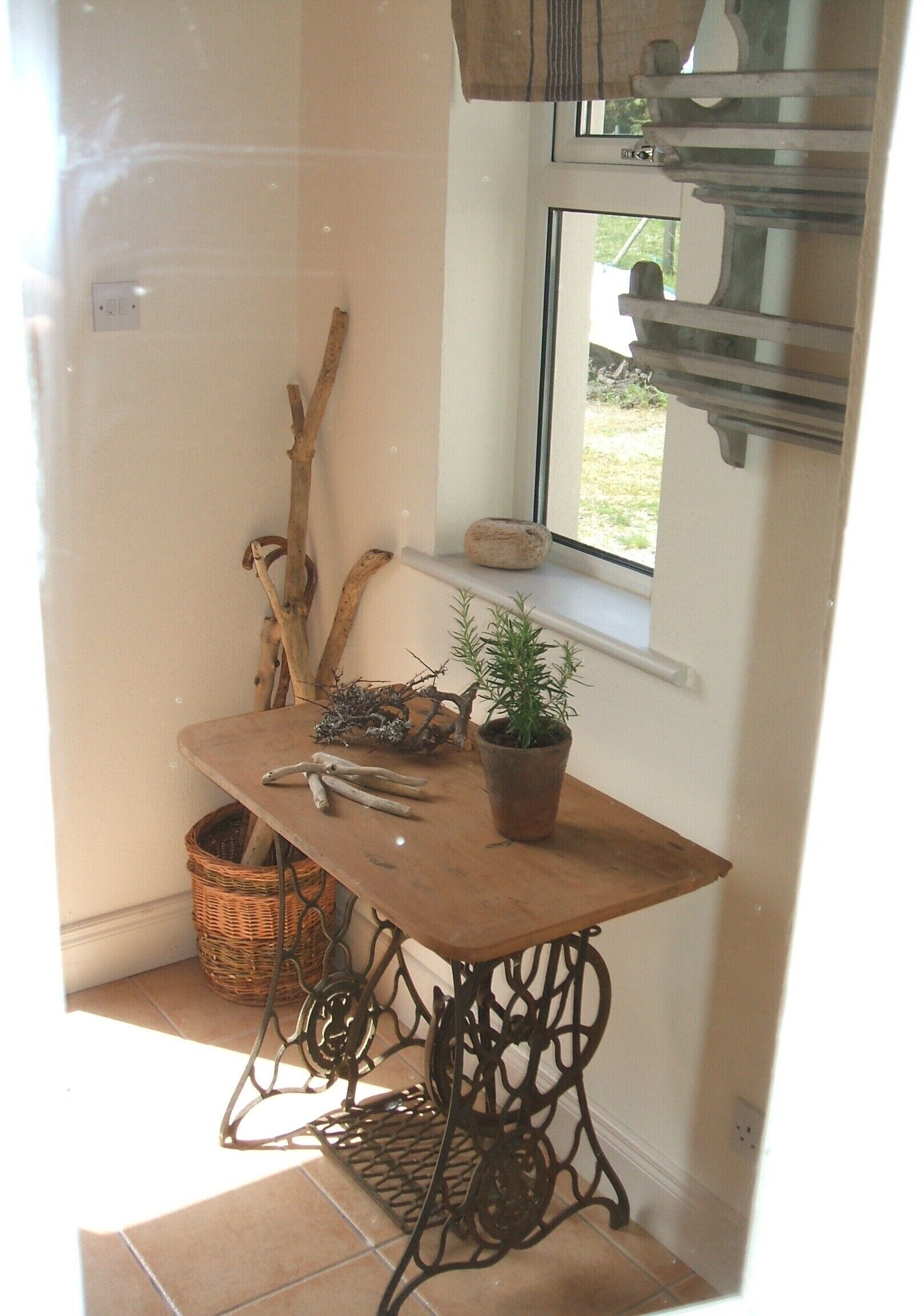 A corner of a room with a wooden table, a potted plant, a wicker basket, and a window with a view of the outdoors.