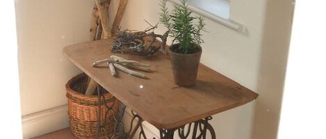 A corner of a room with a wooden table, a potted plant, a wicker basket, and a window with a view of the outdoors.