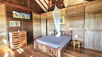 Una habitación con piso de madera, una cama, un tocador, un espejo y un ventilador de techo.