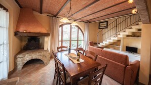 Un comedor acogedor con chimenea de piedra, mesa y sillas de madera. Una escalera conduce a un nivel superior.
