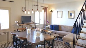 A dining area with a wooden table and chairs, a television on a shelf, and a sofa in the background. - Entire fully renovated town house sea-view rooftop terrace, AC for 6 (Antibes)