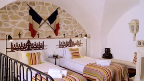 A hotel room with two beds, a stone wall, a decorative metal headboard, a small table, and a nightstand. - Entire fully renovated town house sea-view rooftop terrace, AC for 6 (Antibes)