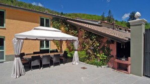 Un patio exterior con un toldo blanco, una mesa con sillas y una zona de barbacoa.