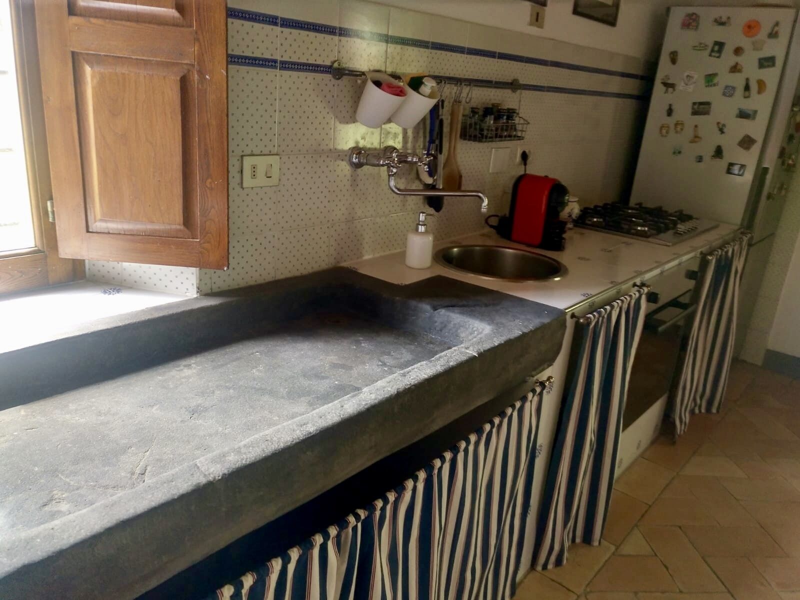 Cucina con piano di lavoro in granito, lavello in acciaio inossidabile e piano cottura rosso.