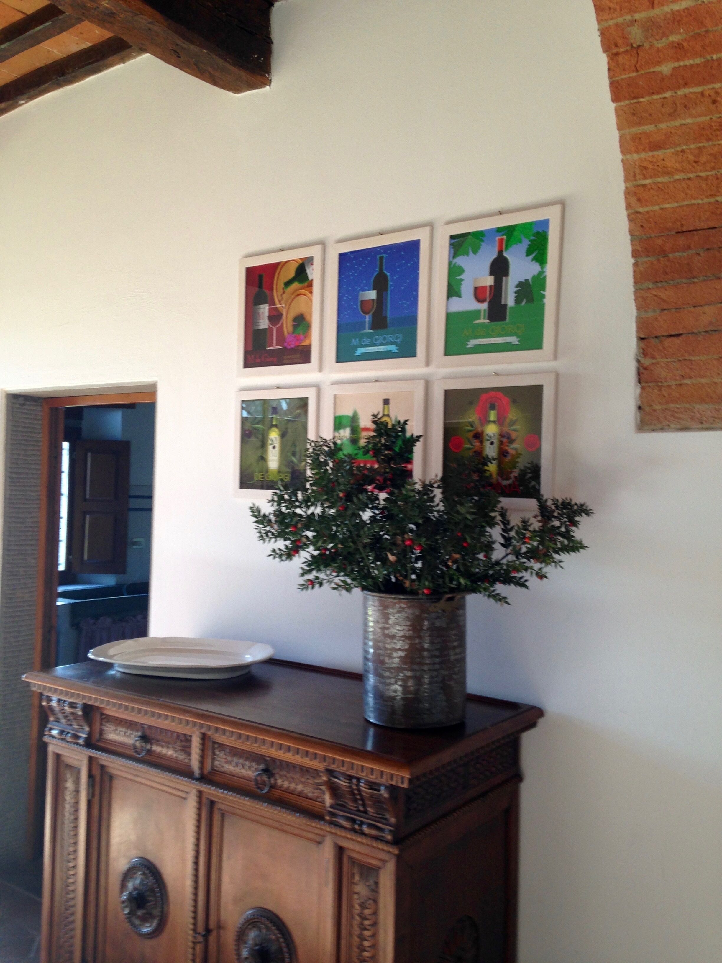 Una pared con seis cuadros enmarcados, una planta en maceta y un mueble de madera con un plato encima.