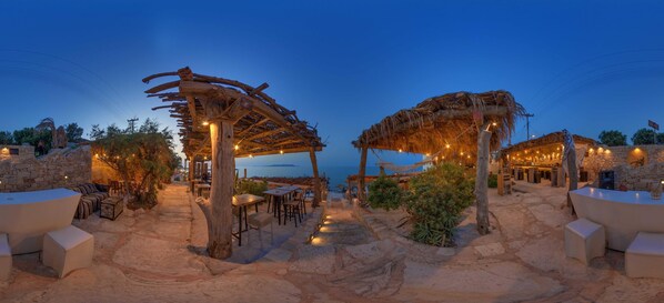 A beachside restaurant with stone walls, outdoor seating, and string lights.
