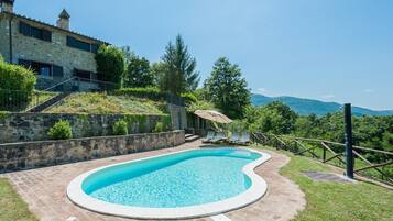 Relax by the serene pool surrounded by lush greenery and a picturesque stone building.
