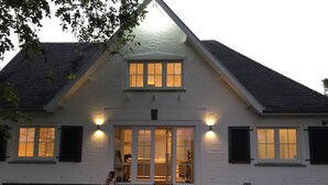 Une maison blanche à deux étages, dotée d’un toit à pignon, d’un porche à l’avant et d’une porte d’entrée à double battant.
