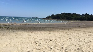 Een strand met boten in het water en mensen die over het zand lopen.