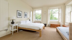Ein Schlafzimmer mit einem Holzbett, einem Nachttisch mit Lampe, zwei gerahmten Bildern an der Wand und einem Fenster mit Blick auf Grünflächen.
