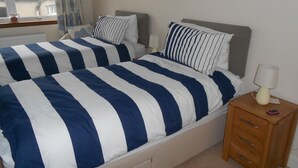 A double bed with striped bedding, a bedside table with a lamp, and a window with curtains.
