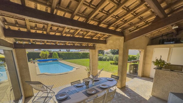 An outdoor patio with a pool, dining table, and chairs.