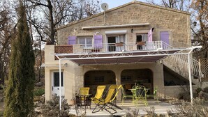 Een stenen huis met een overdekte patio, buitenmeubels en een stenen muur rondom het perceel.